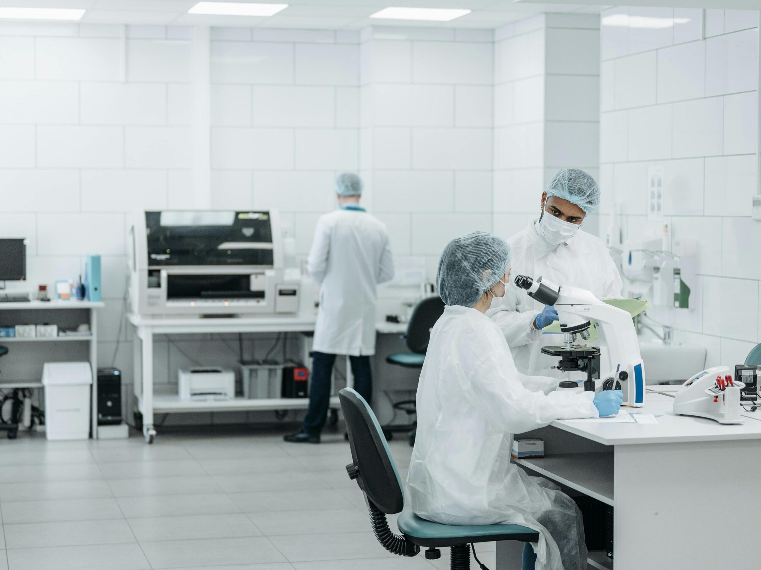 Scientists in protective suits working with microscopes in a well-lit laboratory environment.